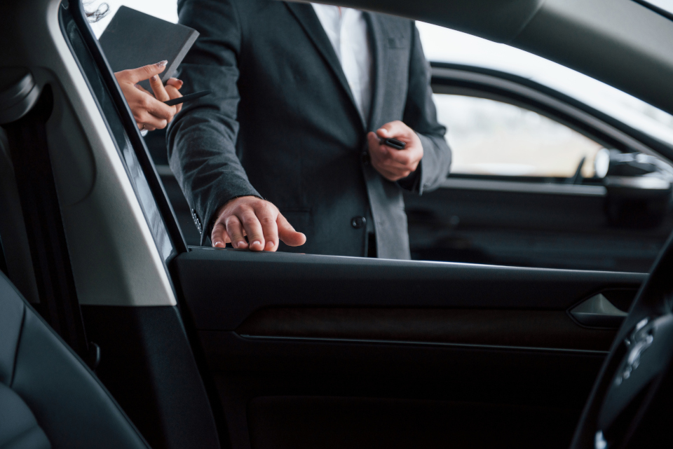 Professional chauffeur in suit opening luxury car door, representing premium limousine reservation service with certified drivers