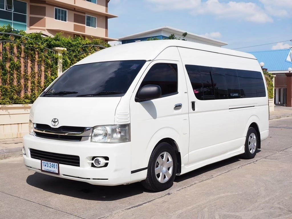 A white van parked on the street in front of a house. It is a limousine used for passenger transport services.