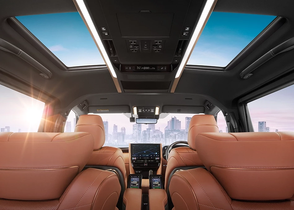 Interior of a luxurious limousine with light brown leather seats, a display screen on the central console, and a panoramic glass roof offering views of the sky and cityscape.